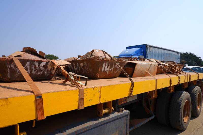 The flatbed of a large trailer with five large copper ingots on them. There are other cars and heavy truck rigs in the background.