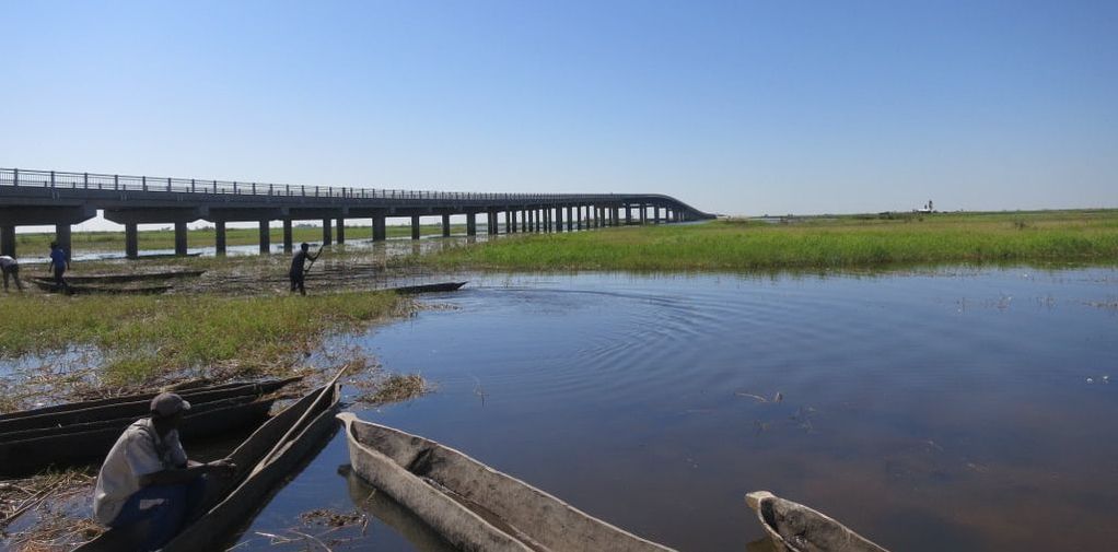 A long bridge over a river with fishermen and canoes in the foreground.