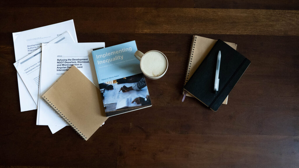 Journal articles, books, notebooks, and a coffee cup on a table, shot from directly above.